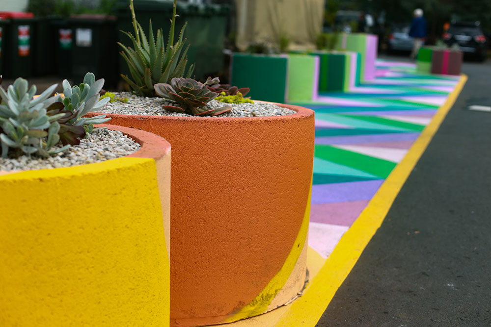 A brightly painted row of planters filled with succulents lines a colourful footpath