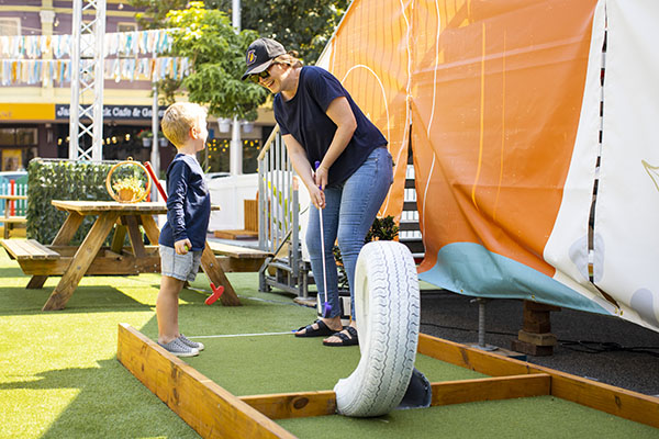 A lady is playing mini golf with a young boy in Subiaco Square