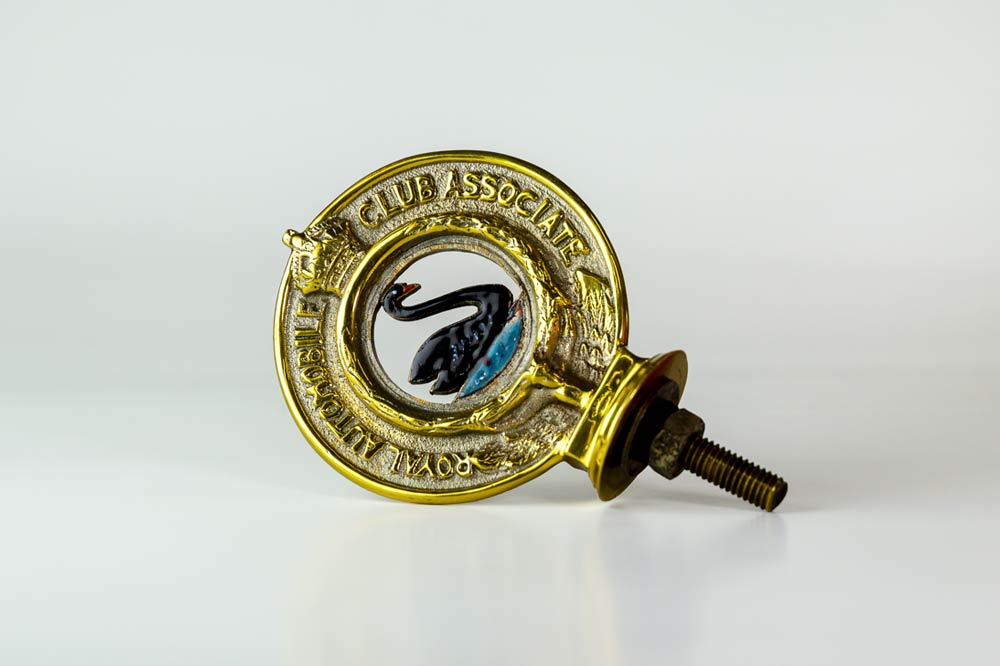 The Automobile Club of WA car badge. Double sided, it reads “Automobile Club of W.A. Incorp.” and on the reverse, “Royal Automobile Club Associate”. In the centre is a black swan swimming on blue water.