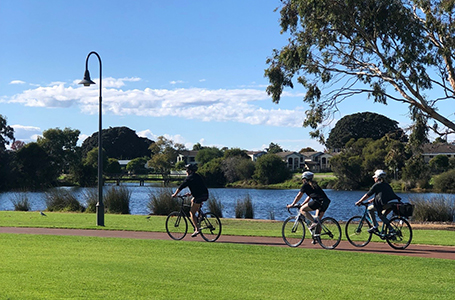 Three people are cycling together next to a river