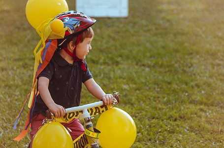 A child is riding a pushbike decorated with yellow balloons'