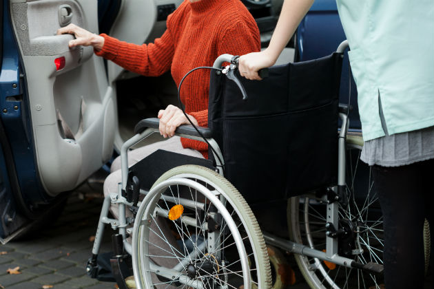 An elderly lady being helped into a car by a carer