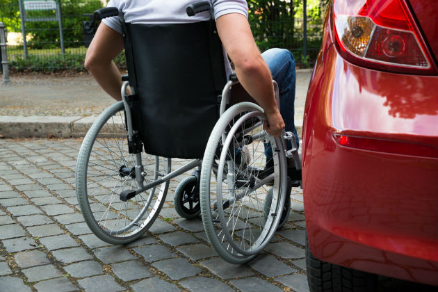 A man in a wheelchair next to a car