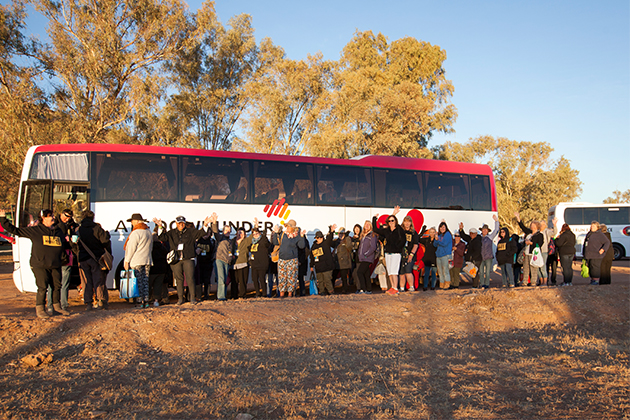 A large tour group wave as they stand in front of their bus