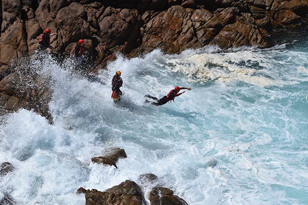 Two people jumping off coastline