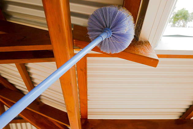 Person using broom to clear cobweb