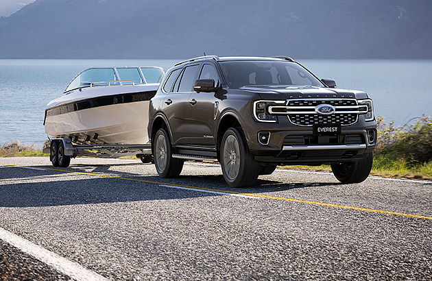A Ford Everest towing a boat on a road with water the background