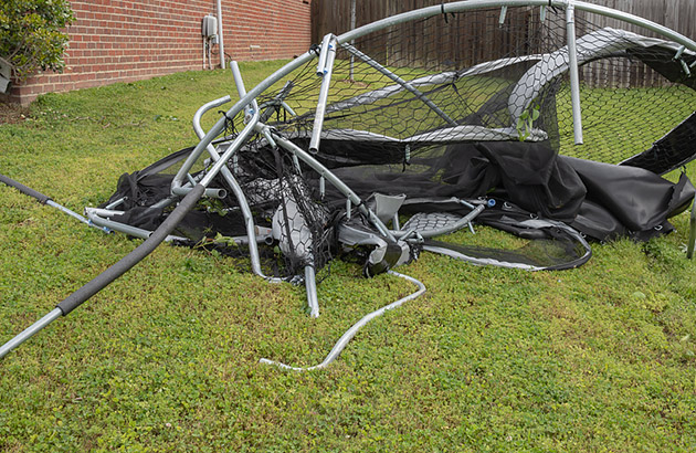 A trampoline destroyed by a storm lying in a backyard