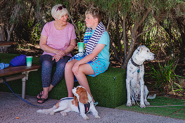 A woman sitting with a young boy with one small and one large dog next to them