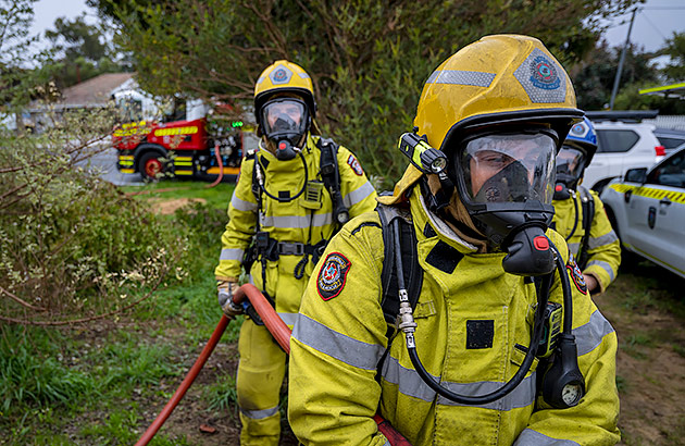 Two fire fighters with breathing apparatus walk towards a house fire