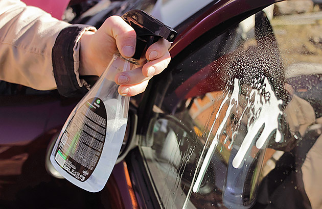 Spraying automotive glass cleaner on a car windscreen