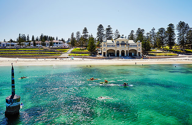 Cottesloe Beach with the water in the foreground and grass terraces and pine trees along the foreshore 