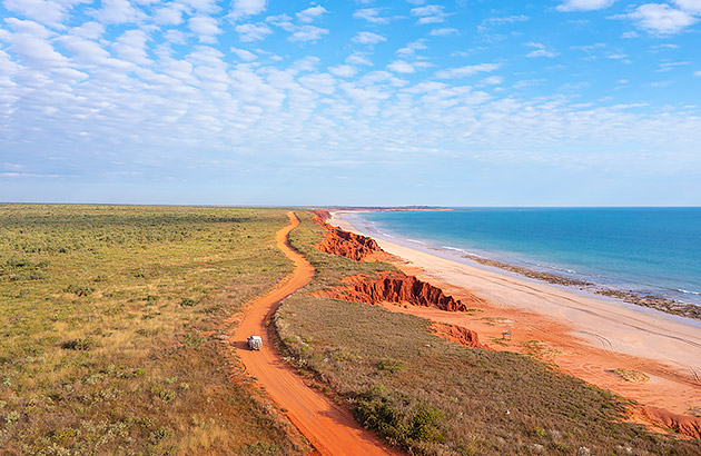 A car on a red dirt track near the ocean near Broome