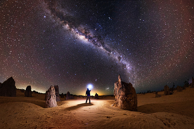 Man holding torch in foreground of night sky at the Pinnacles