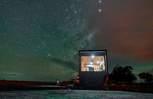 The exterior of a tiny cabin at night showing many stars in the skies above