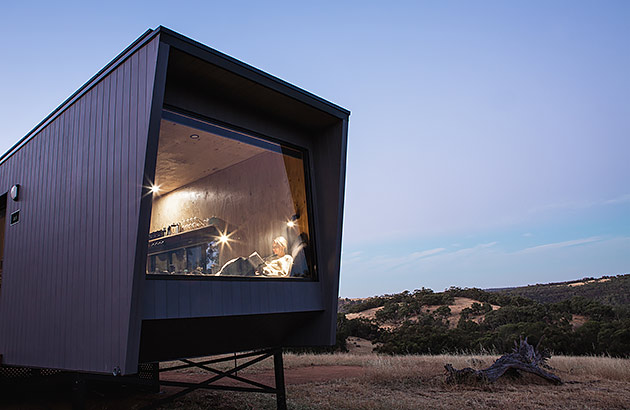 The interior of a tiny cabin showing at night showing a light inside and someone near the window