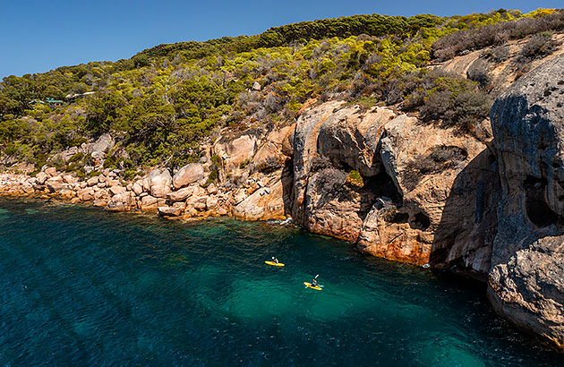 Two kayakers near some large rocks on the Woody Island shoreline