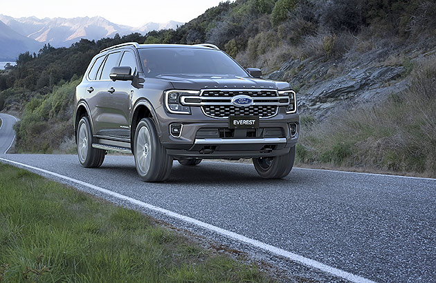 A grey Ford Everest on a winding road with a lake in the background