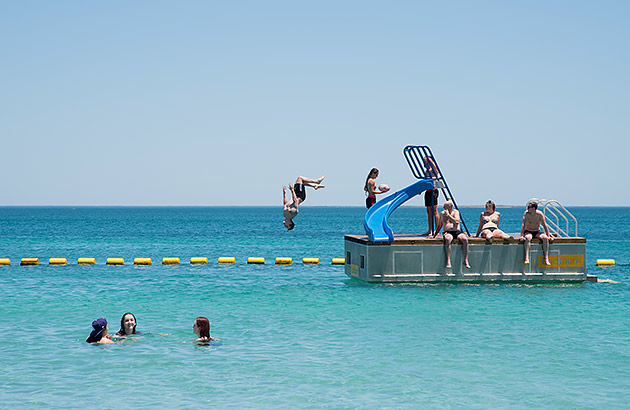 Kids swimming at the beach and one jumping from a pontoon