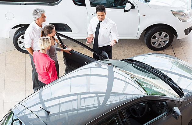 Looking down at four people standing next to a car inside a car showroom