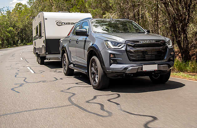 A grey 4WD vehicle towing a caravan on a regional road