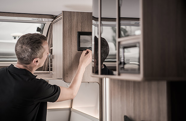 A man inspecting a digital console on the internal wall of a caravan