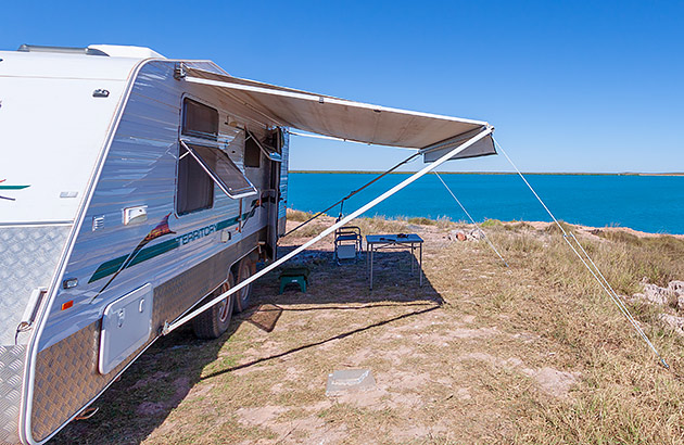 A parked caravan with an awning extended overlooking the ocean