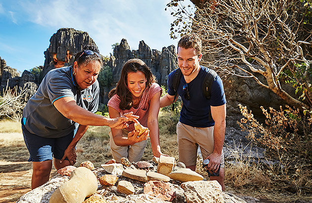 A traditional owner shows some rock tools to a man and woman on a tour