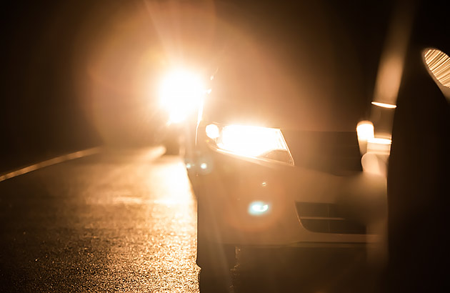 Cars following each other on a dark road with headlights on