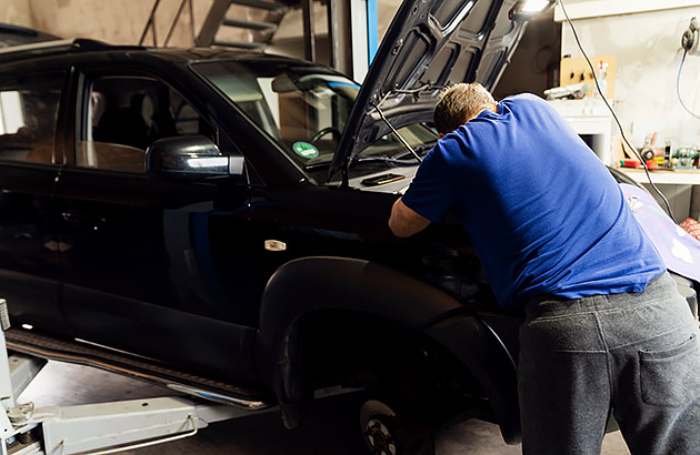 A man in a cluttered workshop works under a car bonnet