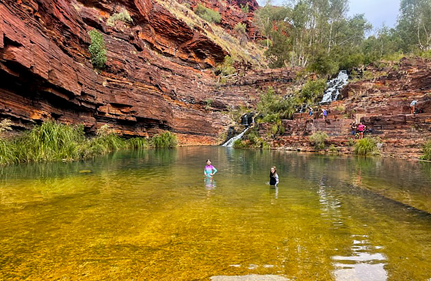 Children swimming and playing near a small waterfall in Karijini National Park