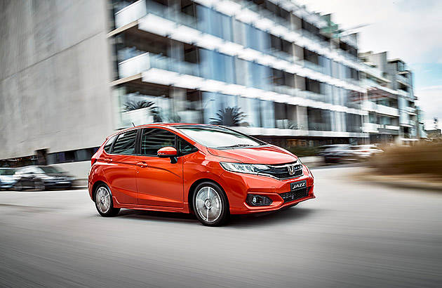 A red Honda Jazz in front of a modern city building