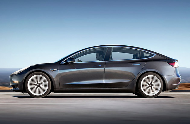 A silver Tesla Model 3 on a road near a beach