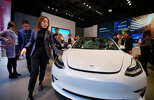 A woman standing beside a white Tesla electric car at a car show
