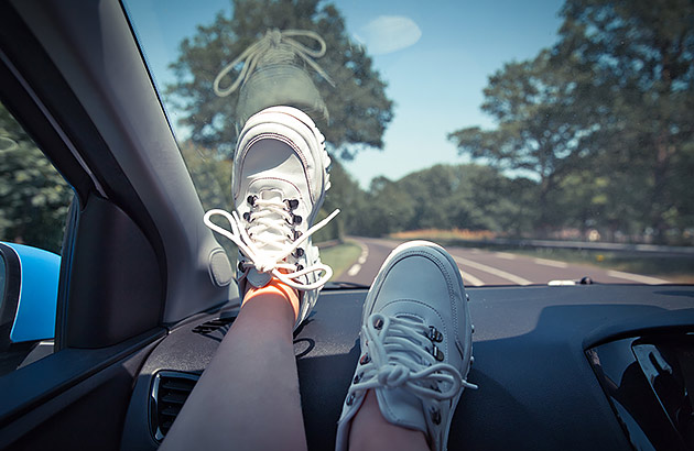 A person's feet up on a car dashboard as the car travels