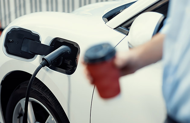 A man holding a take-away coffee while his EV charges