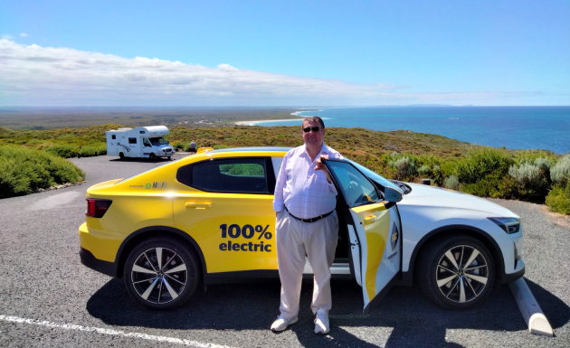 Man standing at open door of Polestar 2 electric car parked with ocean views