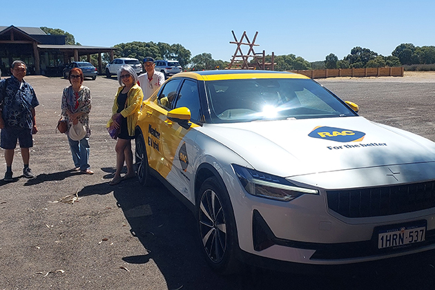 A group of people pose for a photo standing next to a Polestar 2 electric vehicle