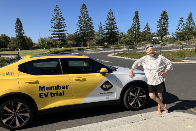 Mid shot of older woman leaning against yellow Polestar 2 electric car in a carpark