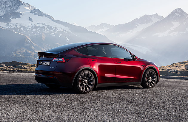 A red Tesla Model Y with a mountainous landscape in the background 