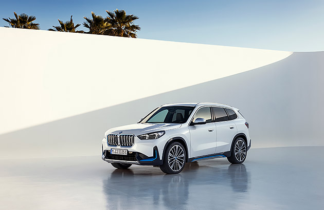 A white BMW iX1 against a tall white wall with sky in the background