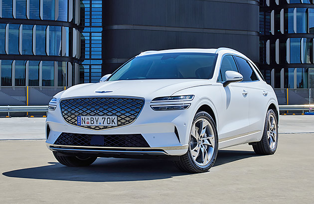 A white Genesis Electrified GV70 parked in front of city buildings