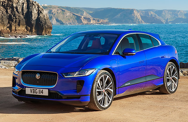 A blue Jaguar I Pace with a rocky coastline in the background