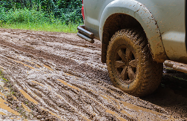 A close up view of a car travelling through mud with mud on the tyres and car body