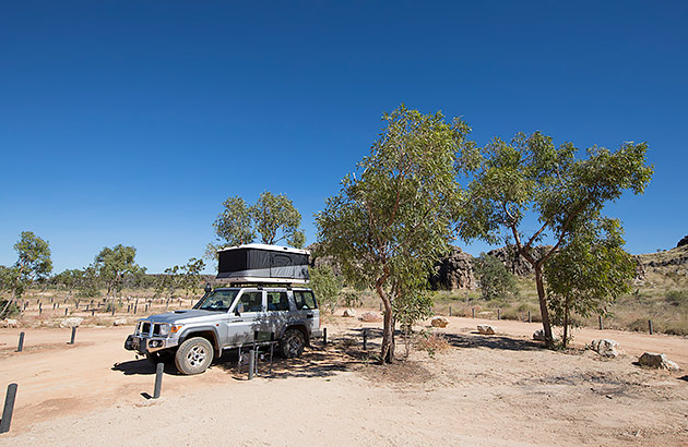 A four-wheel parked near a tree in a bushland clearing with a rooftop tent