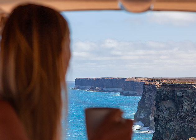 A woman drinking coffee in a campervan overlooking the Great Australian Bight