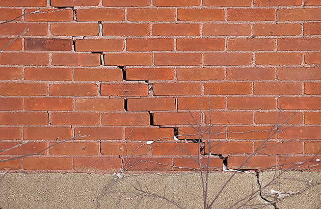 A red brick external house wall with a large crack in a stepped pattern