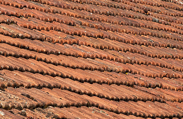 Red tiles on a house roof which is sagging