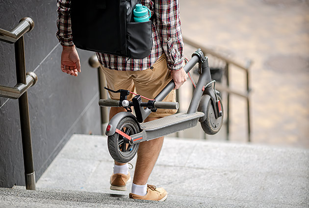 A man carrying a folded e-scooter down a set of stairs