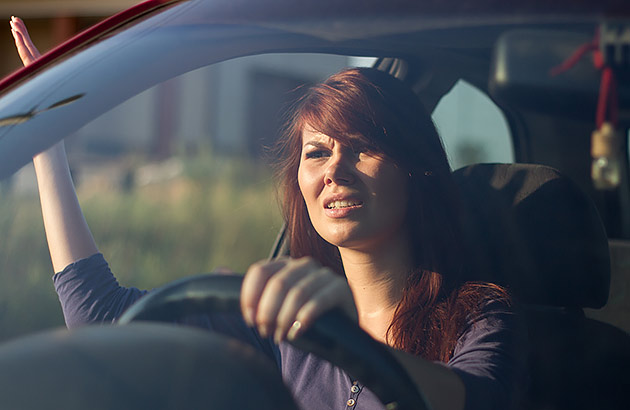 A woman driving a car gestures with her arm to signal anger